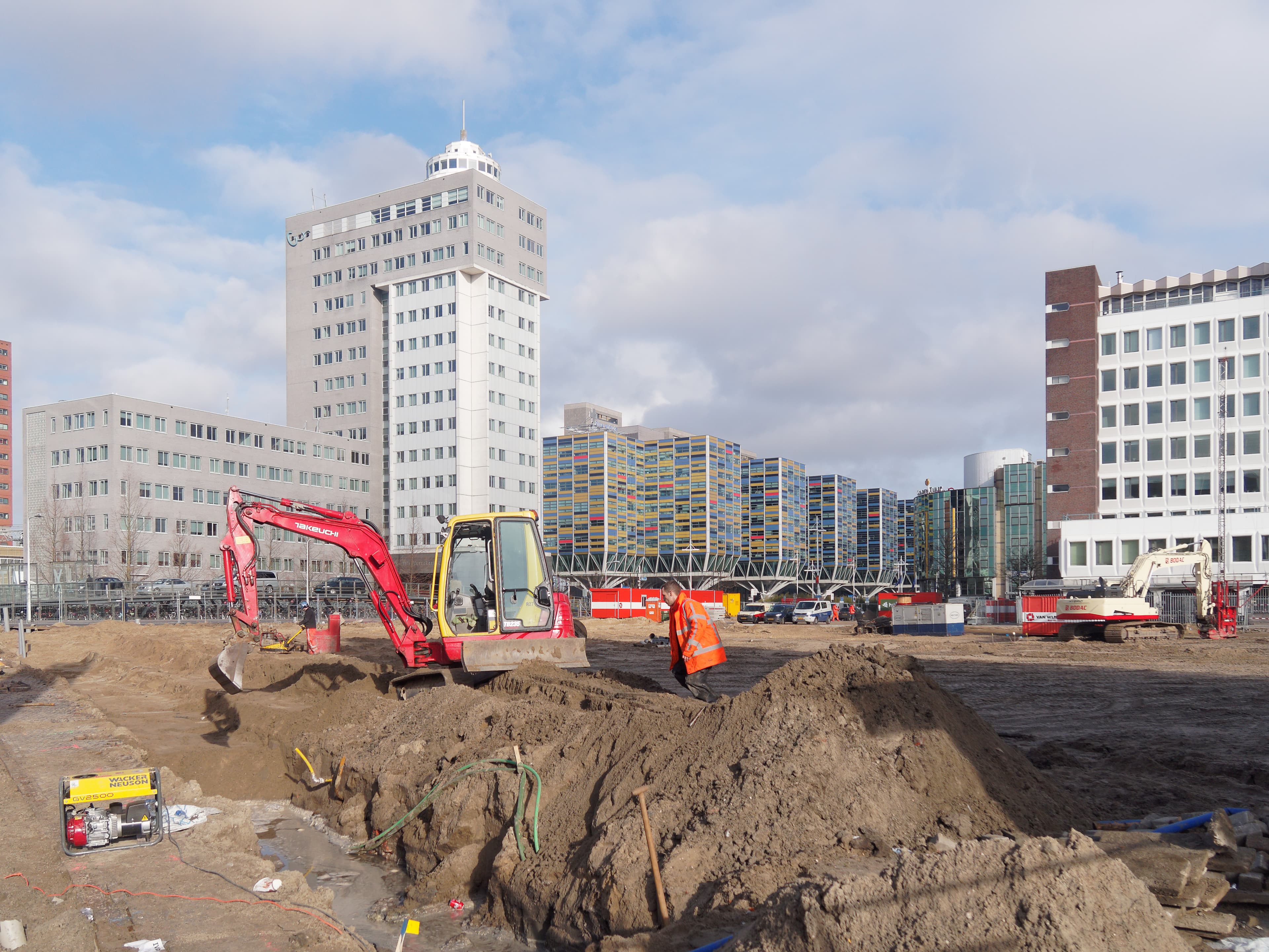 Worker in orange high-vis on an urban construction site with a mini excavator