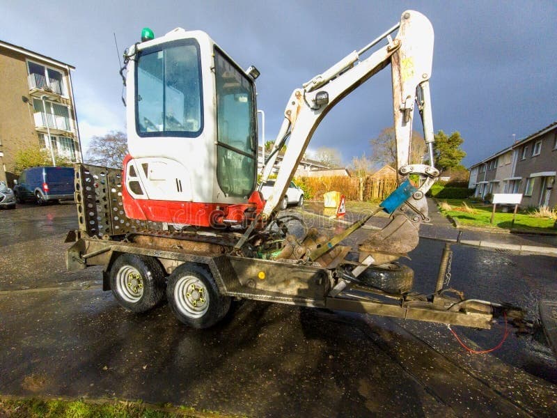 Mini excavator loaded on a tandem-axle plant trailer parked on a residential street